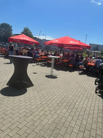 Gäste unter roten Sonnenschirmen auf einem Firmengelände