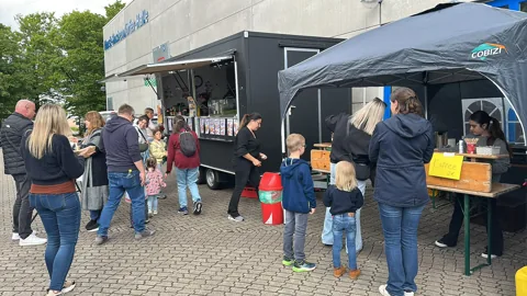 Erwachsene und Kinder warten an der geöffneten Foodtruck-Ausgabe